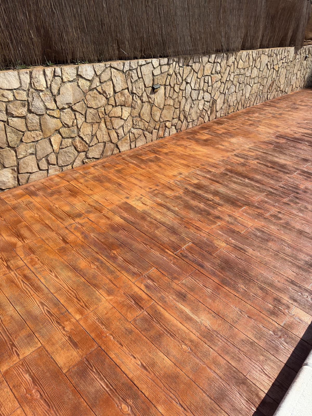 Pavimento impreso imitación madera junto a muro de piedra